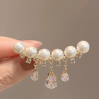 A hand holds a gold-toned hair claw clip decorated with white faux pearls and clear rhinestones, with three dangling clear teardrop crystals. The background is a solid warm gray, and the text 'FUN SHARING' is visible at the bottom.