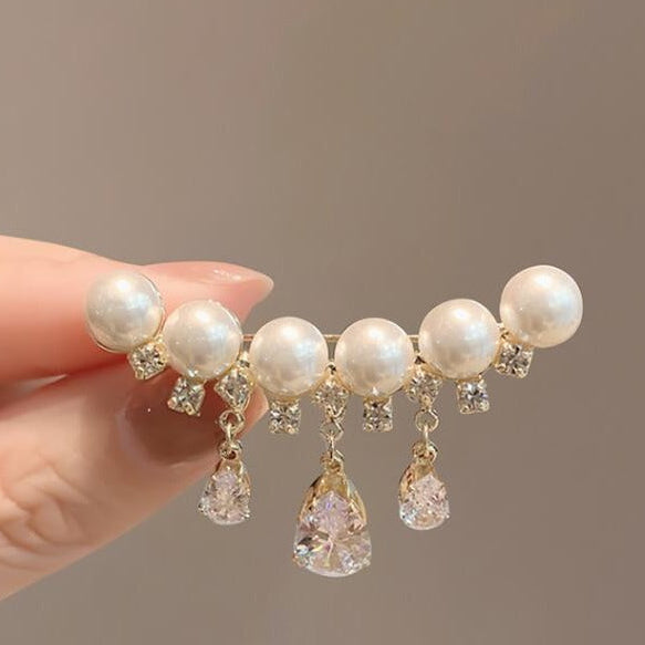 A hand holds a gold-toned hair claw clip decorated with white faux pearls and clear rhinestones, with three dangling clear teardrop crystals. The background is a solid warm gray, and the text 'FUN SHARING' is visible at the bottom.