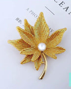 Gold leaf-shaped brooch with a pearl center on a light gray background